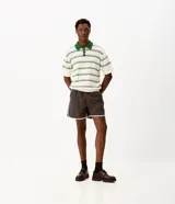 Bermuda deportiva gris oscuro confeccionada en poliamida, de corte corto, con cintura elástica, cordón ajustable y ribetes laterales en color blanco.
