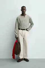 Camiseta de manga larga con cuello panadero (henley) y cierre de tres botones. Presenta un patrón de rayas horizontales finas en tonos beige y negro, con pespuntes a contraste en el cuello, puños y bajo.