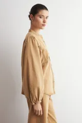 Camisa de jean color camel, de manga larga abullonada, con cuello mao y cierre frontal de botones metálicos.