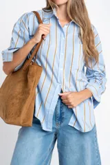 Camisa de corte oversize con estampado de rayas verticales en tonos azul y beige. Presenta cuello camisero clásico, cierre frontal con botones, bolsillo en el pecho y mangas largas con puños rectos.