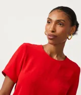 Blusa blanca de poliéster con cuello redondo, mangas cortas, cierre trasero en forma de gota, pequeñas aberturas laterales y acabados en pespuntes en las mangas y el cuello.