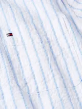 Camisa de manga corta Tommy Hilfiger, confeccionada en algodón BCI con tejido seersucker a rayas blancas y celestes. Tiene cuello clásico, cierre con botones, corte regular y logo bordado en el pecho.