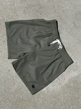 Short de baño verde oliva con estampado geométrico en tono más claro, cintura elástica con cordón blanco y logo pequeño en la pierna izquierda.