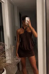 Vestido corto color marrón con diseño de cuello halter, caracterizado por un detalle de argolla circular en el centro del escote y una caída fluida y drapeada en la parte superior, contrastando con una falda ajustada.