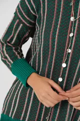 Sweater verde esmeralda de cuello redondo y manga larga, con terminación acanalada en puños y ruedo. Presenta tajos laterales y diseño de rayas verticales en tonos blanco y rosa.