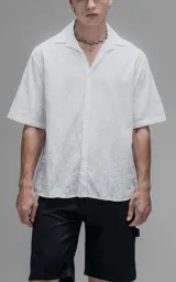 Camisa oversize blanca de manga corta y cuello abierto, confeccionada en algodón con diseño bordado.