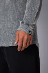 Buzo de corte oversize confeccionado en tela waffle de algodón con proceso de teñido acid wash. Presenta cuello redondo con detalle de costura en X y mangas largas con puños acanalados.