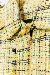 Chaqueta de corte recto confeccionada en tejido con textura de cuadros en tonos amarillos, blancos y negros. Presenta cuello solapa, cierre frontal con botones ocultos, bolsillos de plastrón con solapa en el delantero y mangas largas con puños abotonados.