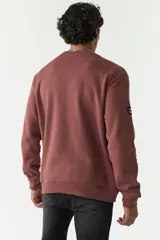 Buzo de felpa verde oliva con logo estampado en el frente, cuello redondo y puños. Confeccionado en 80% algodón y 20% poliéster.