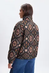 Campera puffer de abrigo con cierre frontal, cuello alto y puños elásticos. Presenta un diseño estampado con motivos geométricos y florales en tonos tierra sobre fondo negro.