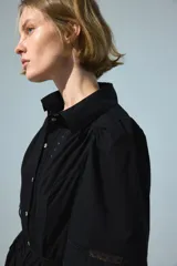 Vestido largo negro de popelina de algodón con alforzas, inserciones de encaje, manga corta abullonada, cuello camisero, botonadura frontal y cinturón fino para atar en la cintura.