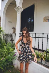 Vestido corto negro con estampado de plumas doradas, escote en V, breteles finos cruzados en la espalda, cut-outs laterales y volado en el ruedo.