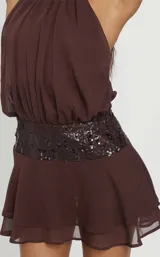 Vestido corto marrón con escote halter fruncido, cintura alta con aplique de lentejuelas y falda con volados en capas.