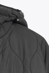 Chaqueta acolchada de color negro con diseño de costuras onduladas, cuello subido y capucha ajustable. Cuenta con cierre frontal de cremallera oculto por una solapa con botones a presión, mangas largas y bolsillos laterales. Tejido con tecnología repelente al agua.