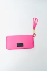 Billetera rectangular color fucsia con cierre perimetral y parche frontal negro con logo. Incluye correa de mano de cordón rosa neón y detalle de ajuste en verde lima.