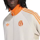 Campera deportiva Adidas Originals del Bayern de Múnich, color beige claro (Wonder Alumina) con detalles en naranja vibrante, cuello alto, cierre frontal y franjas en las mangas.