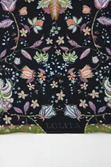 Pañuelo cuadrado de tela fina color negro con estampado floral en tonos pastel y borde verde.