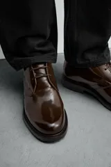 Bota de caña baja tipo chukka, confeccionada en piel con acabado brillante. Presenta cierre de cordones, horma redonda y suela a contraste con ligero tacón.
