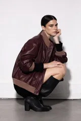 Chaqueta tipo bomber de cuero color bordó, con cuello alto, puños y ruedo de tejido de punto en tono marrón. Presenta cierre frontal con solapa y bolsillos laterales.