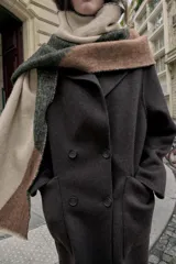 Pañuelo rectangular con diseño color block en tonos beige, gris oscuro y marrón. Presenta una textura tejida y acabados deshilachados en los bordes.