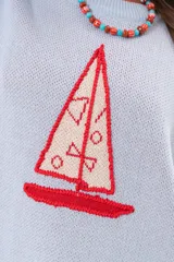 Buzo de punto color celeste con cuello redondo y diseño frontal de un velero tejido en tonos rojos y blancos, con detalles bordados a mano.