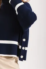 Sweater azul marino de punto con cuello alto, mangas largas con puños blancos y detalle de botones en el lateral.