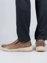 Zapato tipo slip-on Hush Puppies modelo Hunt, confeccionado en cuero color marrón con suela de EVA y goma en tono beige. Presenta elásticos laterales para facilitar el calce y un diseño de estilo casual.