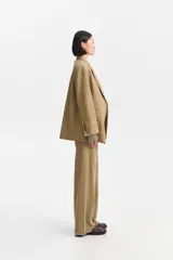 Pantalón de corte relajado y pierna ancha, color marrón claro o camel, con costuras exteriores visibles y terminación deshilachada en el bajo.