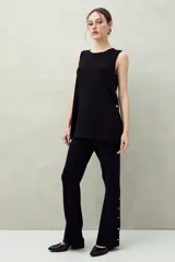 Pantalón blanco de tejido de punto, corte ancho y fluido, con botones dorados decorativos en la costura lateral exterior de ambas piernas.