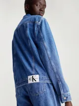 Campera de jean azul medio de corte clásico, con cuello en punta, bolsillos de parche en el pecho, bolsillos de hendidura en la cintura, botones metálicos de la marca y logo de Calvin Klein en el bolsillo del pecho.
