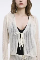 Cardigan tejido de punto calado color blanco, con mangas largas y cierre frontal con lazos.