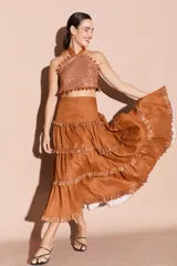 Falda larga de lino color tostado, con diseño de volados escalonados decorados con detalles brillantes en los bordes. Presenta una silueta fluida y cintura alta.