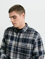 Camisa de franela a cuadros con cuello button-down, manga larga y botones de madera. Presenta dos bolsillos tipo parche en el frente con cierre de botón.