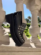 Mocasines de cuero negro con plataforma y suela de goma, decorados con tachas metálicas plateadas en el empeine y el talón.