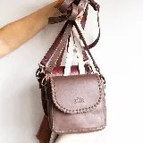 Mini cartera bandolera de cuero, de formato compacto y diseño atemporal con solapa frontal y costuras artesanales decorativas en el borde. Cuenta con el logotipo de la marca grabado en la parte delantera y correa larga regulable.