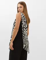 Enterito de seda fría con pantalón palazzo de corte ancho y fluido. Presenta un diseño asimétrico con una tira fina en un hombro y un detalle de herraje metálico en el otro, del cual se desprende una capa de gasa estampada con patrón abstracto en blanco y negro.