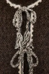 Chaqueta de punto de textura bouclé en color marrón oscuro, con cuello redondo y manga larga. Presenta detalles de vivo a contraste en color crema en los bordes y cierre frontal mediante lazadas decorativas con flecos.