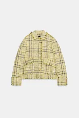 Chaqueta de corte recto confeccionada en tejido con textura de cuadros en tonos amarillos, blancos y negros. Presenta cuello solapa, cierre frontal con botones ocultos, bolsillos de plastrón con solapa en el delantero y mangas largas con puños abotonados.
