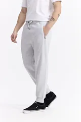 Pantalón de jogging color gris melange, confeccionado en tejido de algodón y poliéster. Presenta cintura elástica con cordón de ajuste, bolsillos laterales con cierre y puños elásticos en los tobillos.