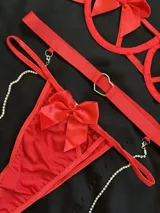 Conjunto de lencería rojo compuesto por soutienne con aros y moños decorativos, bombacha vedetina con letras de strass y tiras regulables, y portaligas con arnés y cadenas de brillantes.