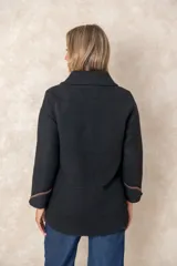 Chaqueta negra de corte amplio y diseño estructurado, con cierre frontal de botones. Presenta bolsillos frontales y puños con ribetes en contraste color marrón.