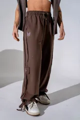 Pantalón de estilo urbano color marrón, con cintura elástica ajustable mediante cordón, bolsillos laterales y bajos ajustables con tiras. Presenta un pequeño estampado en la pierna.