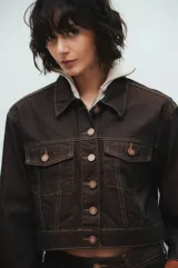 Campera de jean cropped color marrón oscuro, con costuras en contraste color beige, bolsillos con solapa, botones metálicos y puños rebatidos color marrón claro.