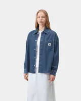 Camisa de denim azul de corte holgado, con cuello clásico, cierre frontal de botones metálicos y bolsillo parche en el pecho con etiqueta cuadrada de la marca.