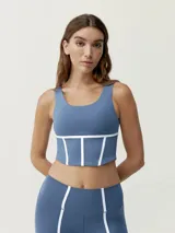 Top deportivo cropped de sujeción media, color azul, con escote caja y tirantes anchos. Presenta vivos blancos a contraste que simulan un estilo corsé en la parte inferior.
