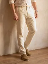 Pantalón de lino color beige, de corte recto, con bolsillos laterales y traseros. Se ajusta a la cintura con cinturón de cuero marrón.
