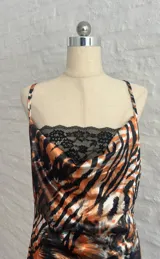 Minivestido ajustado con estampado animal print en tonos naranja, marrón y negro. Diseño con escote drapeado con detalle de encaje negro y tirantes finos.