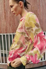 Blusa de manga larga con estampado floral en tonos rosados, verdes y beige. Presenta escote en pico con detalle de abalorios colgantes y cierre frontal con botones.