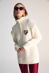 Buzo color crudo de algodón pima, con cuello alto con botones y detalle bordado de corazón en el pecho.