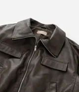 Campera tipo bomber de cuero sintético en color marrón oscuro, con cuello inglés, cierre frontal de cremallera, bolsillos laterales y bolsillos frontales con solapa.